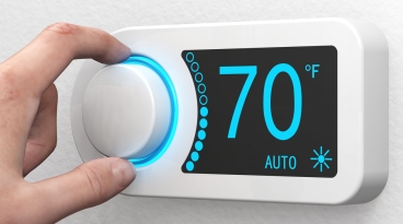 Radiator Mounted Thermostat Person's fingers adjusting the knob on a room's wall mounted thermostat.