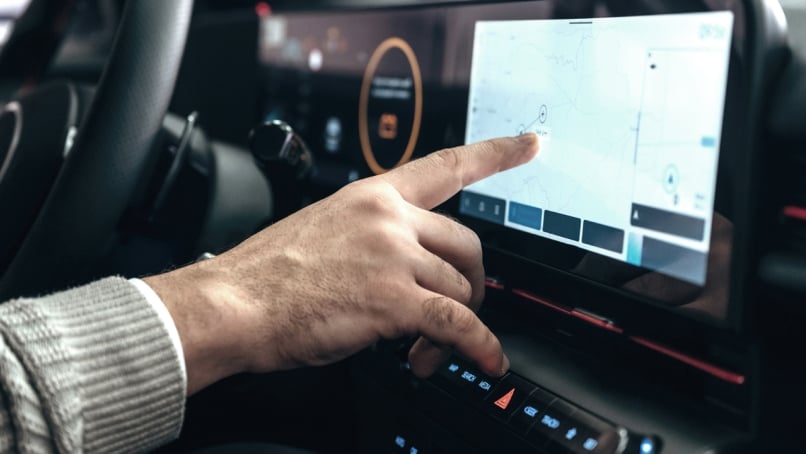 Finger touching a car's infotainment screen to navigate maps.